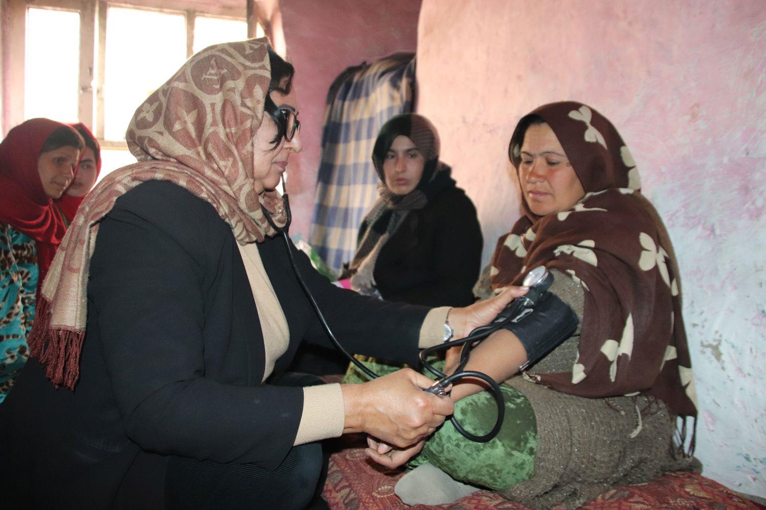 Frau misst einer Frau den Blutdruck in Afghanistan, während drei anderen Frauen zuschauen