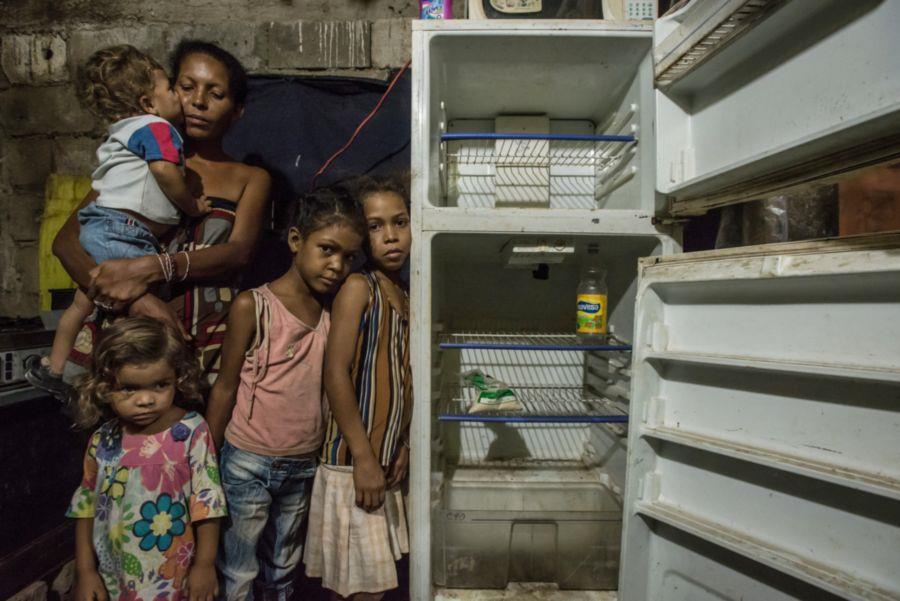 Eine Frau und ihre Kinder stehen vor einem leeren Kühlschrank