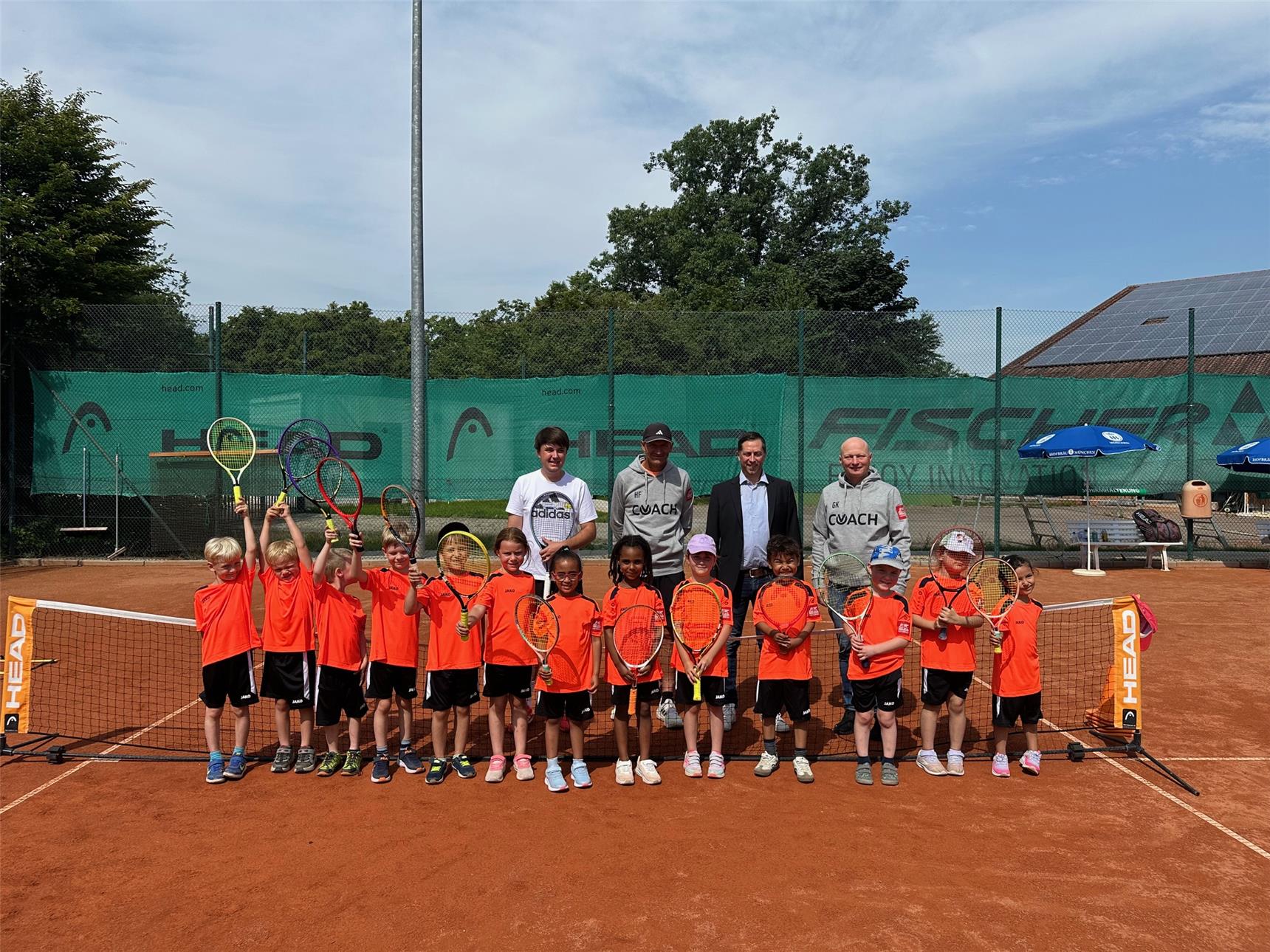 Eine Gruppe von Kindern posiert für ein Foto auf einem Tennisplatz.
