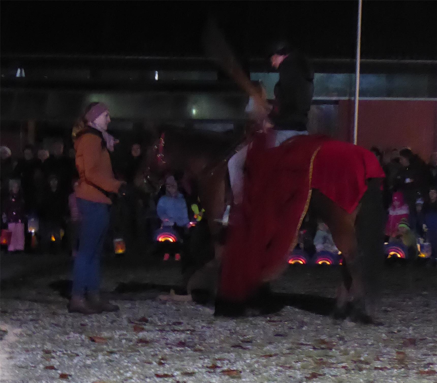 Ein Mann auf einem Pferd mit rotem Umhang, während eine Frau am Boden steht und ihn ansieht.
