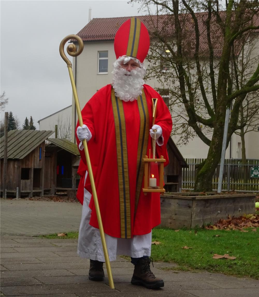 Ein Mann in einem Nikolaus-Kostüm hält eine brennende Kerze in der Hand und lächelt freundlich in die Kamera.