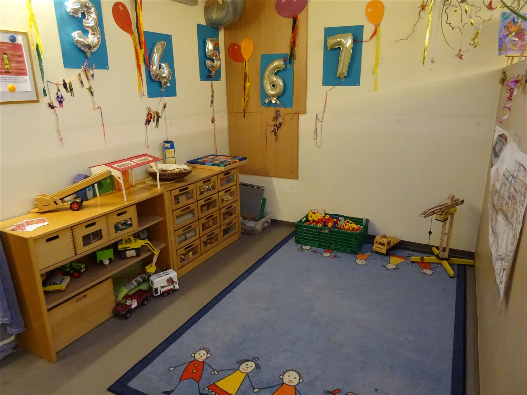 Spielecke mit buntem Teppich. Es gibt viel Spielzeug und bunte Bilder an der Wand