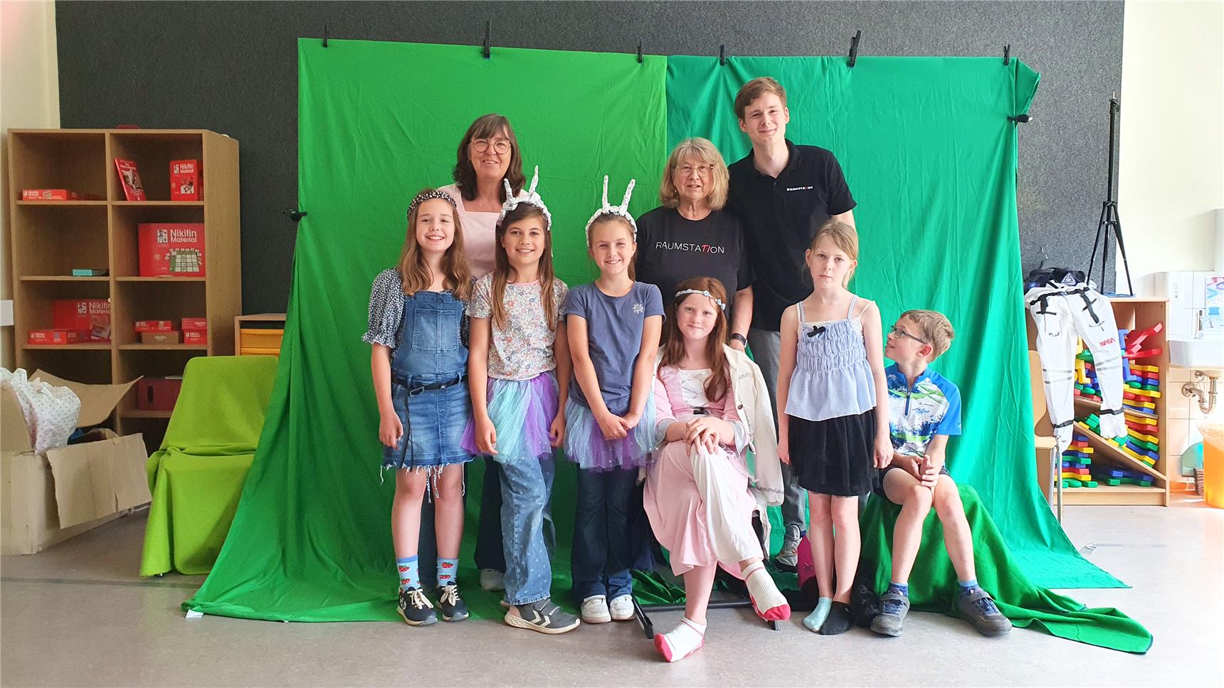 Frau Telaak (links hinten), Dagmar Nieke und Till Nieke (rechts hinten) mit den Kindern der OGS Rees vor dem Greenscreen. Für das Projekt „Raumstation“ der Firma „Diskurs Niederrhein“ lernen die Kinder, wie man Filme dreht und eigene Szenen gestaltet.