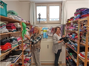 zwei Frauen sortieren Kleider in Kleiderkammer an Regalen