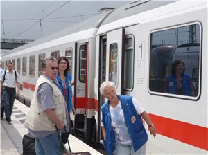 Bahnhofsmitarbeiterinnen helfen älterem Mann mit Gepäck am Gleis