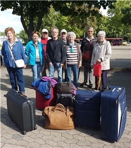 Mehrere Seniorinnen und Senioren mit Koffern vor Abfahrt in ihre Freizeit
