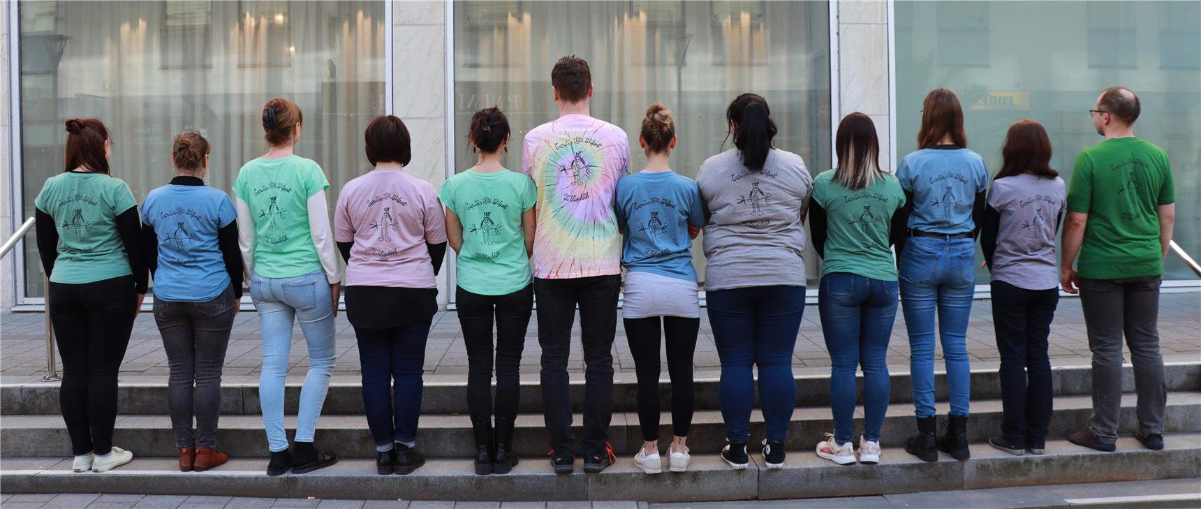 12 Personen mit dem Rücken zum Betrachter, deren T-Shirts alle die selbe Aufschrift "Kita Elifant - St. Elisabeth" tragen