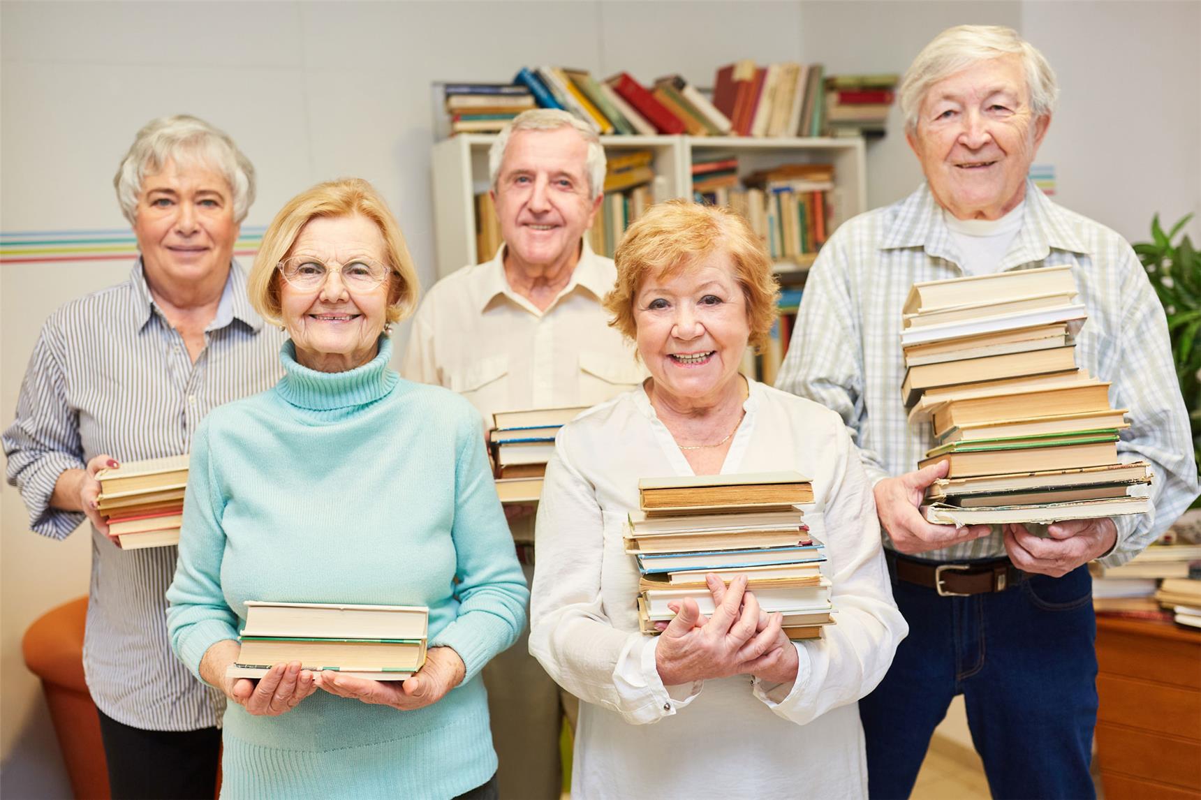 Fünf Seniorinnen und Senioren schauen lächelnd mit Bücherstapeln in den Händen zum Betrachter