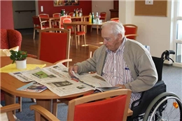 Älterer Herr im Rollstuhl beim Zeitunglesen im großen Gemeinschaftsraum 