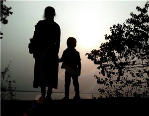 Eine Frau steht Hand in Hand mit ihrem Kind im Sonnenuntergang auf einem Hügel