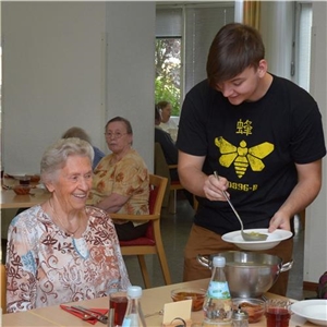 Ein junger Mann füllt für eine Seniorin Suppe auf einen Teller.