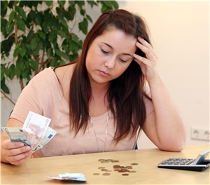 Eine junge Frau mit besorgtem Gesicht sitzt an einem Tisch und zählt Geld.