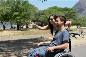 junger Mann im Rollstuhl mit Begleiterin auf Reisen
