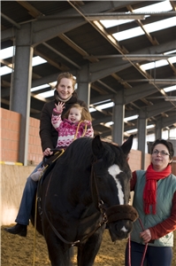 Eine Mutter mit ihrem kranken Kind auf einem Pferd bei der Reittherapie
