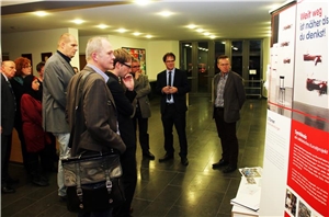 Man sieht auf dem Bild mehrere Personen links auf dem Bild vor der Ausstellung stehen.