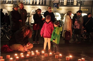 Das Foto zeigt Kinder und Erwachsenen, die vor ihnen aufgestellte Kerzen betrachten, ein Mann sitzt auf dem Boden und zündet eine Kerze an.