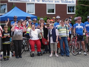 Das Foto zeigt eine Gruppe von Menschen vor einem Banner, zum einen Bewohner eines Behindertenwohnheims und dazu Rennradfahrer in Montur.