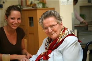 Auf dem Bild sitzt eine Pflegerin neben einer älteren Dame