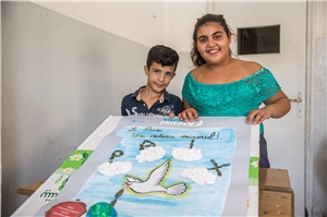 Zwei syrische Flüchtlingskinder präsentieren den von ihnen gestalteten Friedensvertrag mit Wolken, Olivenzweigen und einer kleinen Weltkugel