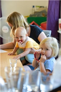 Das Foto zeigt eine Mutter mit zwei Kindern an einem Tisch, die schreibt.