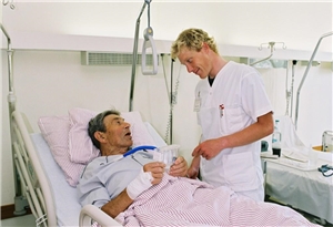 Das Foto zeigt einen Krankenpfleger, der mit einem Patienten im Krankenbett spricht.