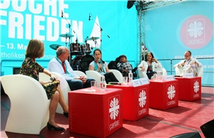 Das Foto zeigt eine Gruppe Menschen, die in weißen Stühlen in einer Reihe auf einer Bühne sitzen.
