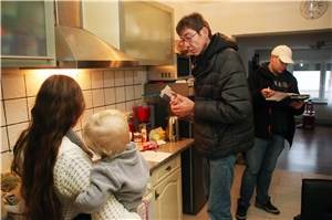 Das Foto zeigt zwei Männer, die in einer Küche mit einer Frau sprechen.