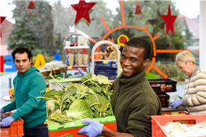 Das Foto zeigt einen jungen Afrikaner mit einer Kiste voll Salat in einem Geschäft.