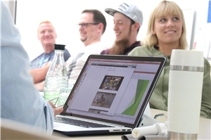 Teilnehmer des Kurses sitzen zusammen, der Kursleiter hält eine Präsentation über seinen Laptop