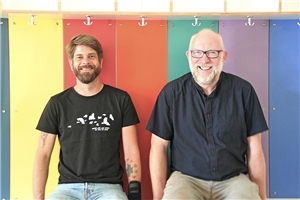 Gruppenleiter, Manuel Mackowiak und Teamberater, Ralf Neier, sitzen vor einer bunt gestalteten Wand, die Teil des Farbkonzeptes darstellt