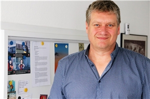 Das Foto zeigt als Poträt vor einer bunt bestückten Pinwand Frank Müller.