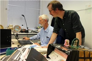 Zwei Herren schauen auf einen Laptop in einem überfüllten Büro.