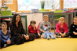 Das Foto zeigt eine Lehrerin mit Grundschulkindern, die in einem Kreis sitzen