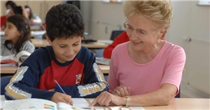 Das Foto zeigt eine ältere Frau, die einem Schüler bei seinen Hausaufgaben hilft.