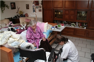 Das Foto zeigt eine Pflegekraft am Bett einer älteren Patientin in ihrer Wohnung.