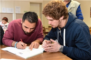 Das Foto zeigt einen Mann, der einem Flüchtling hilft, ein Papier auszufüllen. 