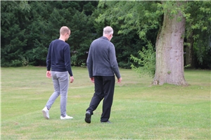 Das Foto zeigt zwei Männer, die nebeneinander über einen Rasen laufen.