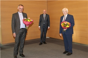 Dr. Christian Schmitt, Heinz-Josef Kessmann und Josef Leenders stehen beisammen. Schmitt und Leenders haben Blumen in den Händen.