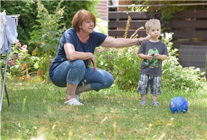 Das Foto zeigt eine Mutter, die mit einem kleinen Kind auf dem Rasen spielt.