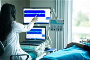 Das Foto zeigt eine Pflegekraft an einem Krankenbett, die einen Monitor bedient.