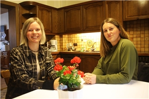Das Foto zeigt zwei Frauen, die an einem Tisch in einer Küche sitzen.