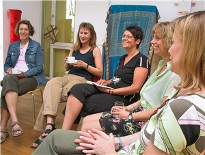 Das Foto zeigt eine Gruppe Frauen, die im Kreis sitzen und Spaß miteinander haben.