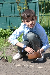 Das Foto zeigt einen Jungen auf dem Boden hockend und aus einer Schüssel Samen säend.