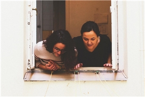 Das Foto zeigt zwei junge Frauen, die sich aus einem Fenster beugen.