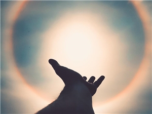 Das Foto zeigt eine Hand, die in den Himmel zur Sonne zeigt.