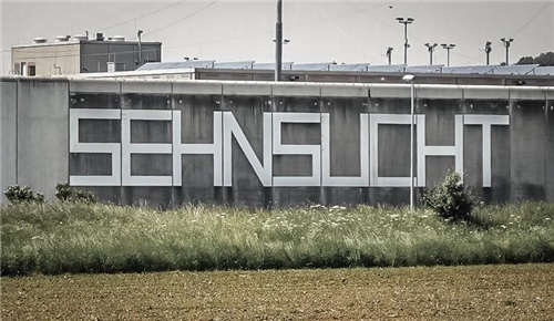 Juli 2018 - Sehnsucht im Kopf Auf einer grauen Wand steht "Sehnsucht" geschrieben.