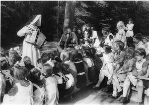 Das Foto zeigt eine Ordensschwester, die einer Schar Kinder vor ihr Akkordeon vorspielt.