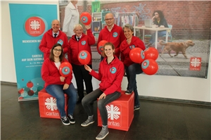 Das 6-köpfige Vorbereitungsteam des Caritasverbandes für die Diözese Münster hat rote Caritas-Jacken an und hält rote Caritas-Luftballons hoch.