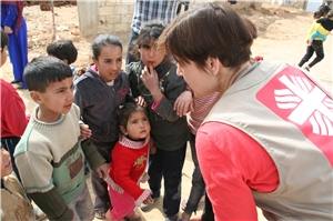 Das Foto zeigt eine Mitarbeiterin der Caritas, die sich zu einer Gruppe von Flüchtlingskindern herunterbeugt