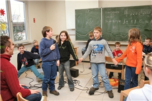 Grundschulkinder musizieren mit verschiedenen Instrumenten in einer Klasse vor der Tafel.